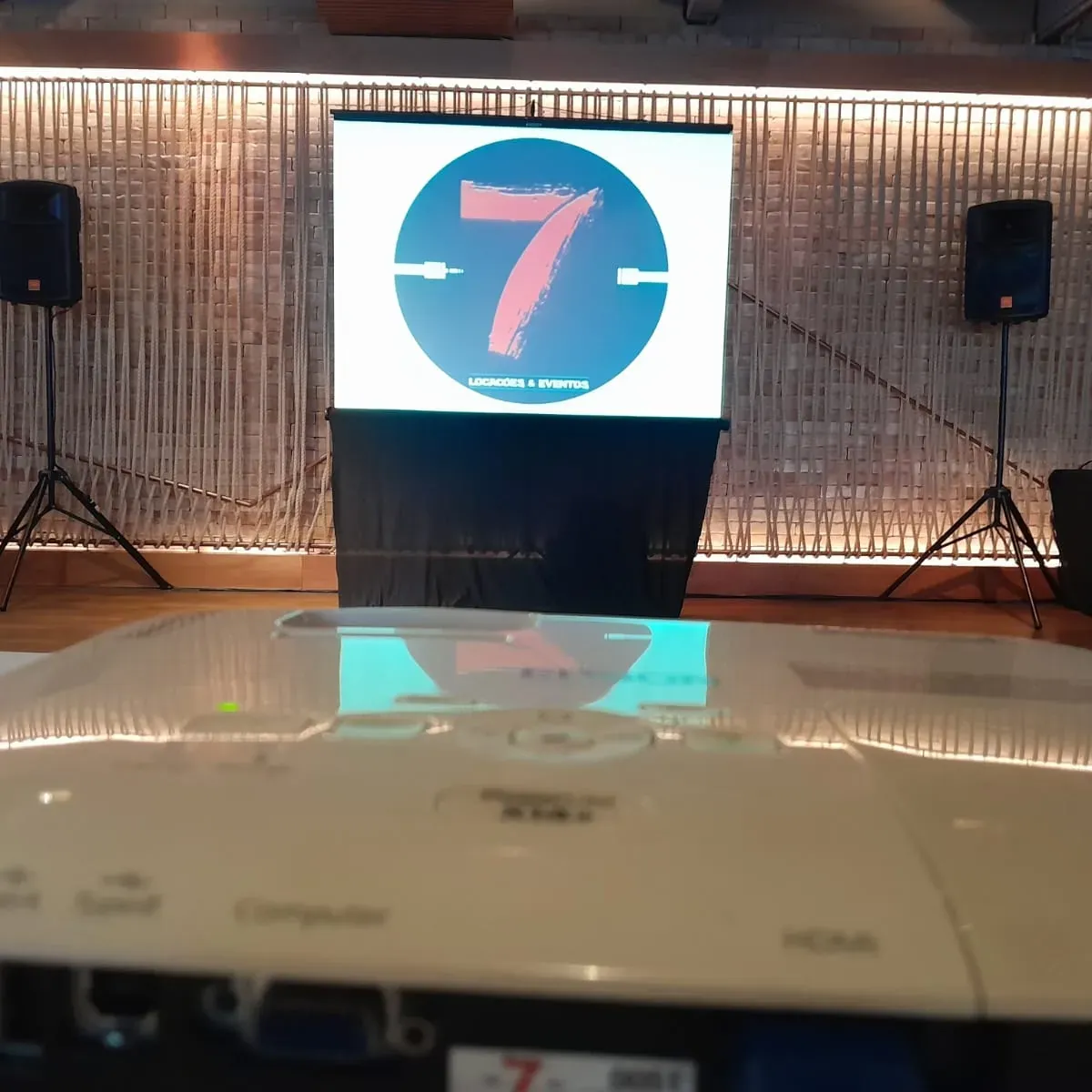Tela de projeção e duas caixas de som montadas em um espaço de eventos